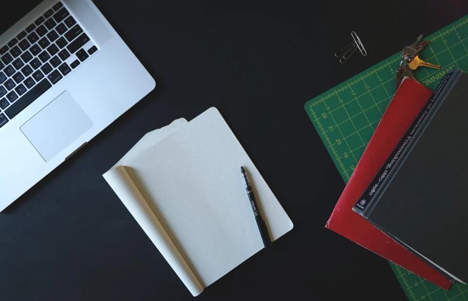 Cuaderno abierto y ordenador sobre una mesa oscura